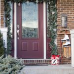 Simple Christmas front porch decorations a vintage touch. Create a pretty holiday porch with garland, lights and a vintage sled draped with ice skates!
