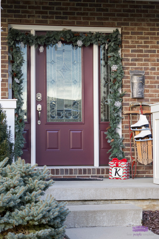 Simple Christmas front porch decorations a vintage touch. Create a pretty holiday porch with garland, lights and a vintage sled draped with ice skates!